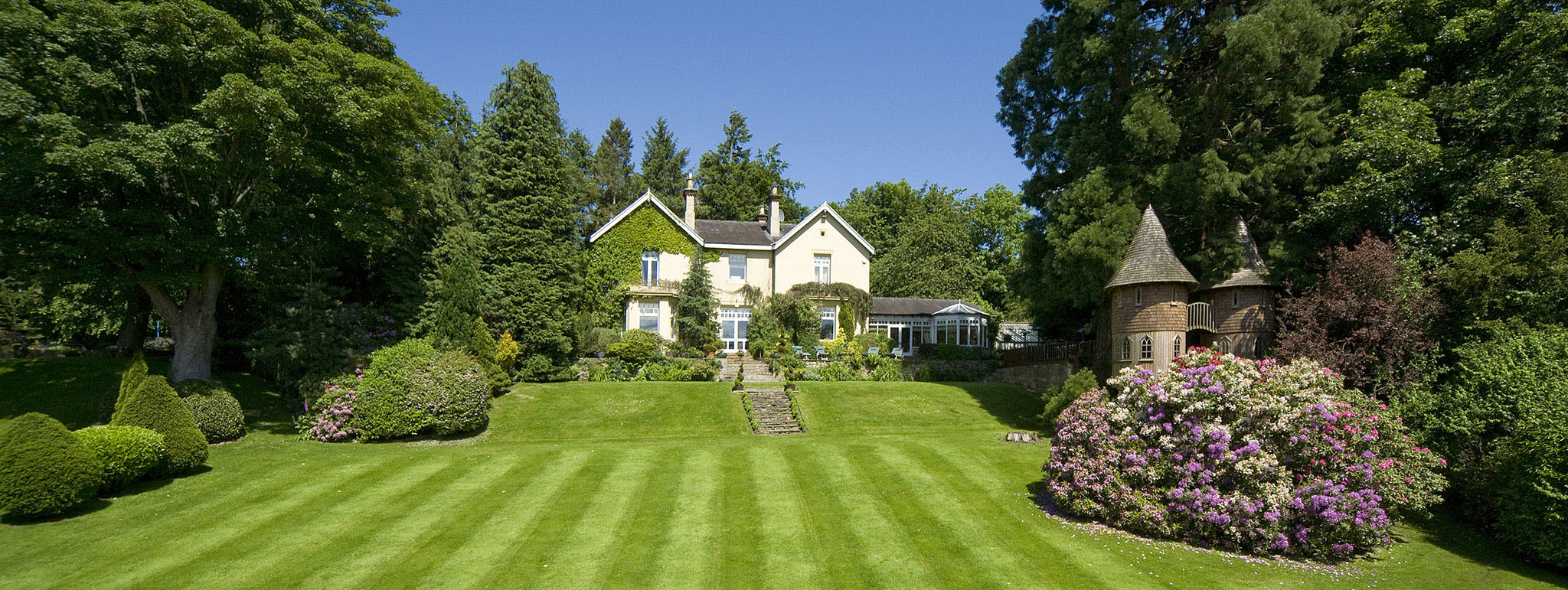 Architectural exterior of property set into gardens with treehouse