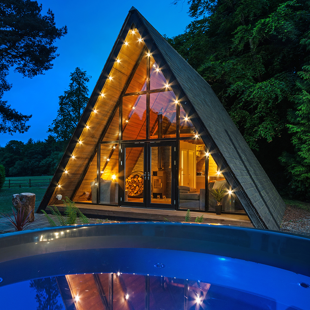 Exterior of a-frame garden building at dusk with hot tub