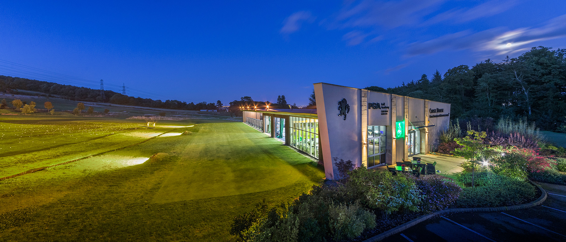Exterior of a golf club academy taken towards the driving range at dusk