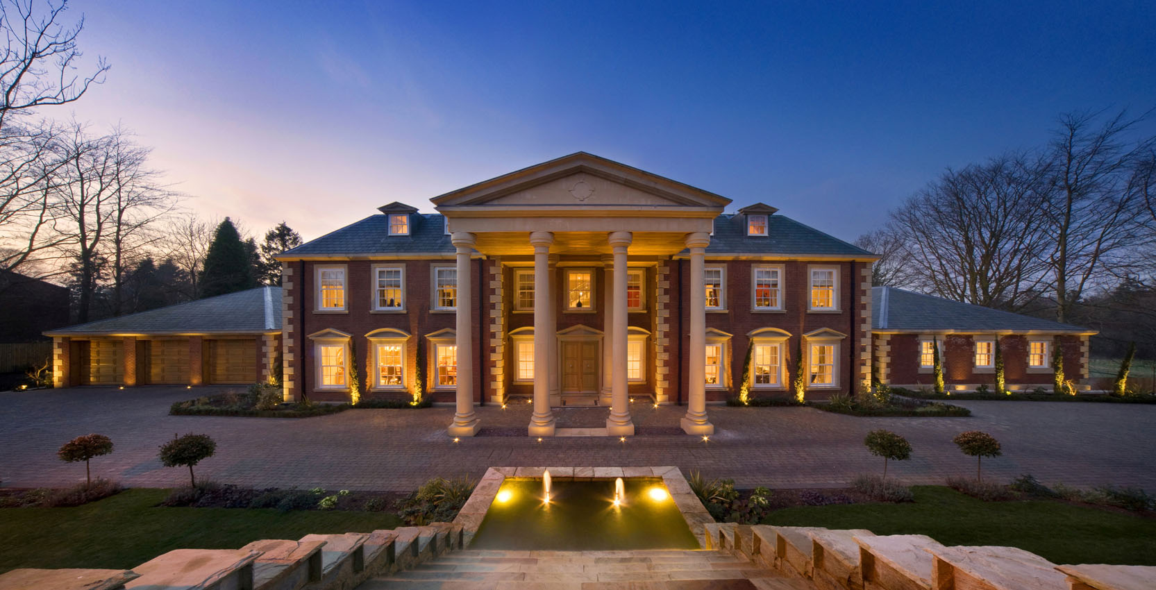 Architectural exterior of a large residential property at dusk overlooking a fountain
