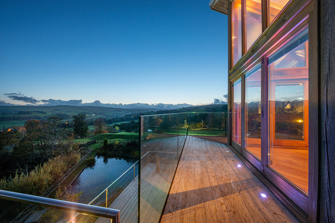Exterior of a residential property with large glass windows overlooking the countryside at dusk