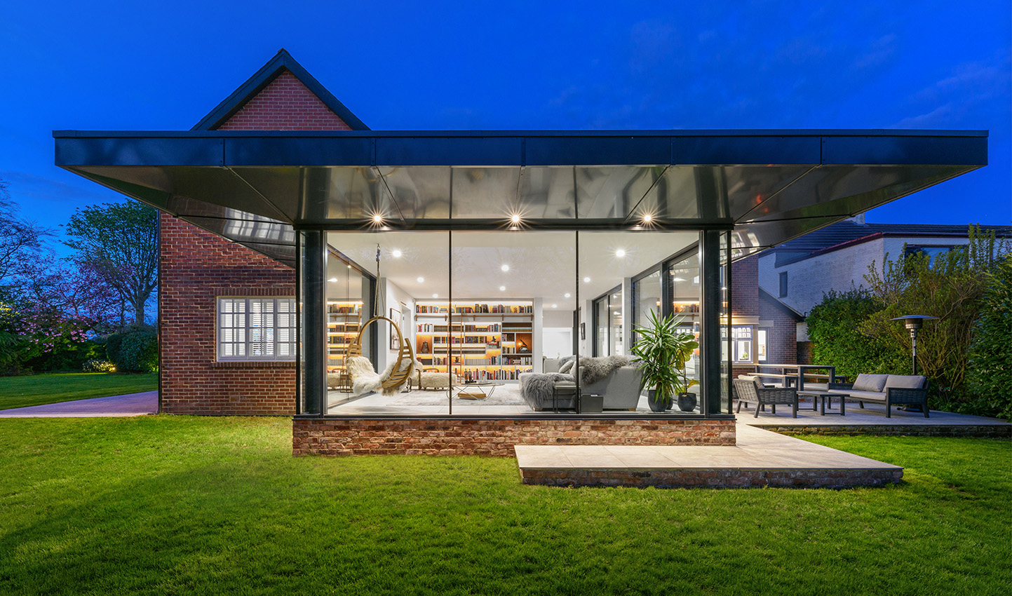 Architectural exterior of a residential glass summer room at dusk with a view into the interior
