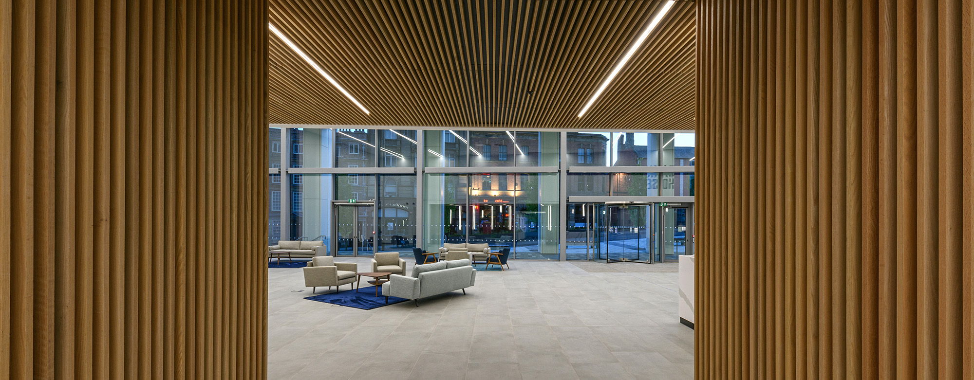 Interior of a commercial office building with wooden design features looking towards a glazed area at dusk