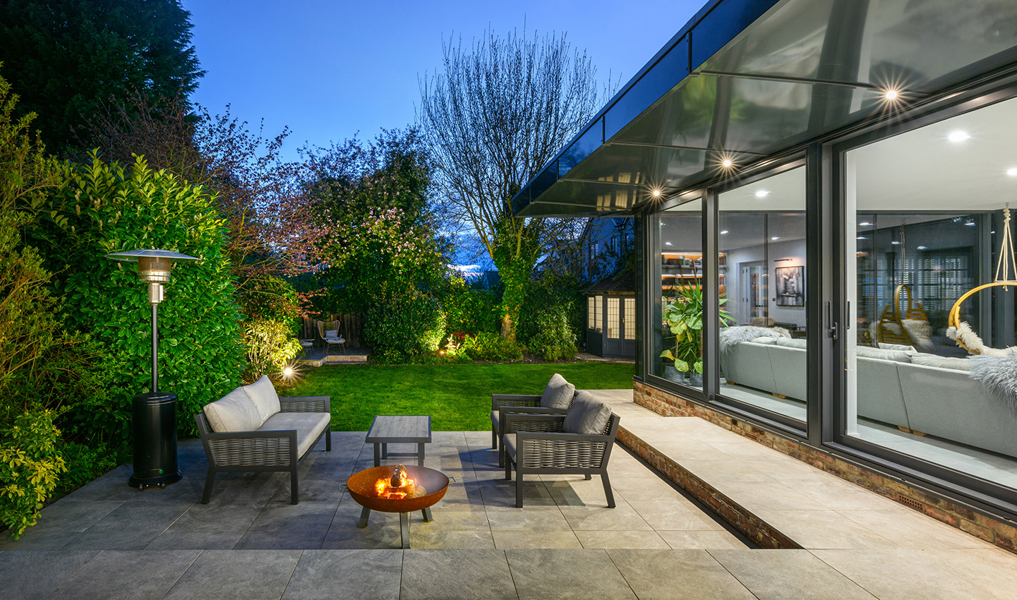 Garden and glazed room wall at dusk with fire pit 