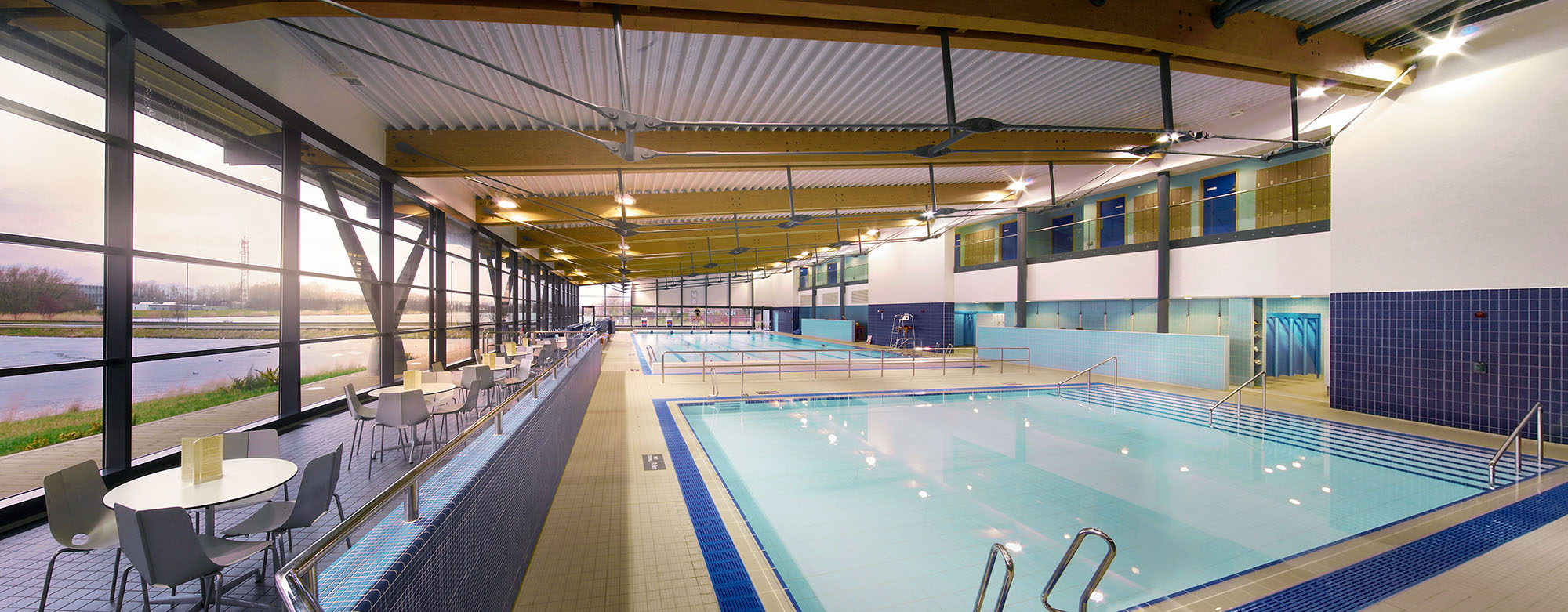 Interior of a large indoor swimming pool and seating area with views out of glazed walls 