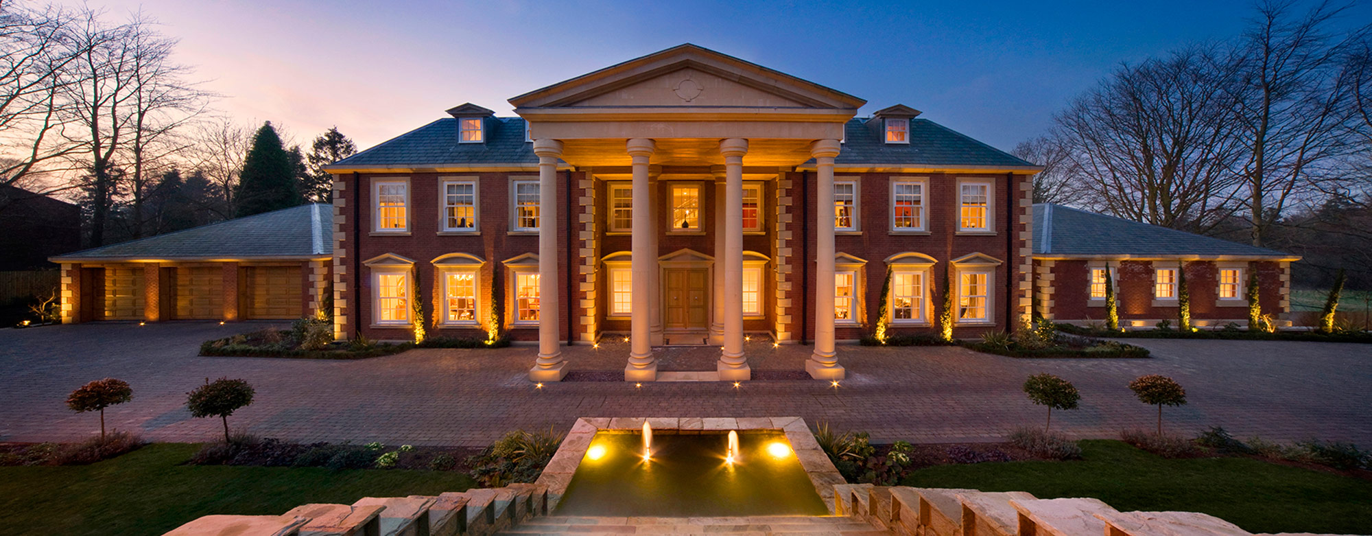 Architectural elevation of a illuminated grand residential property at dusk with blue sky
