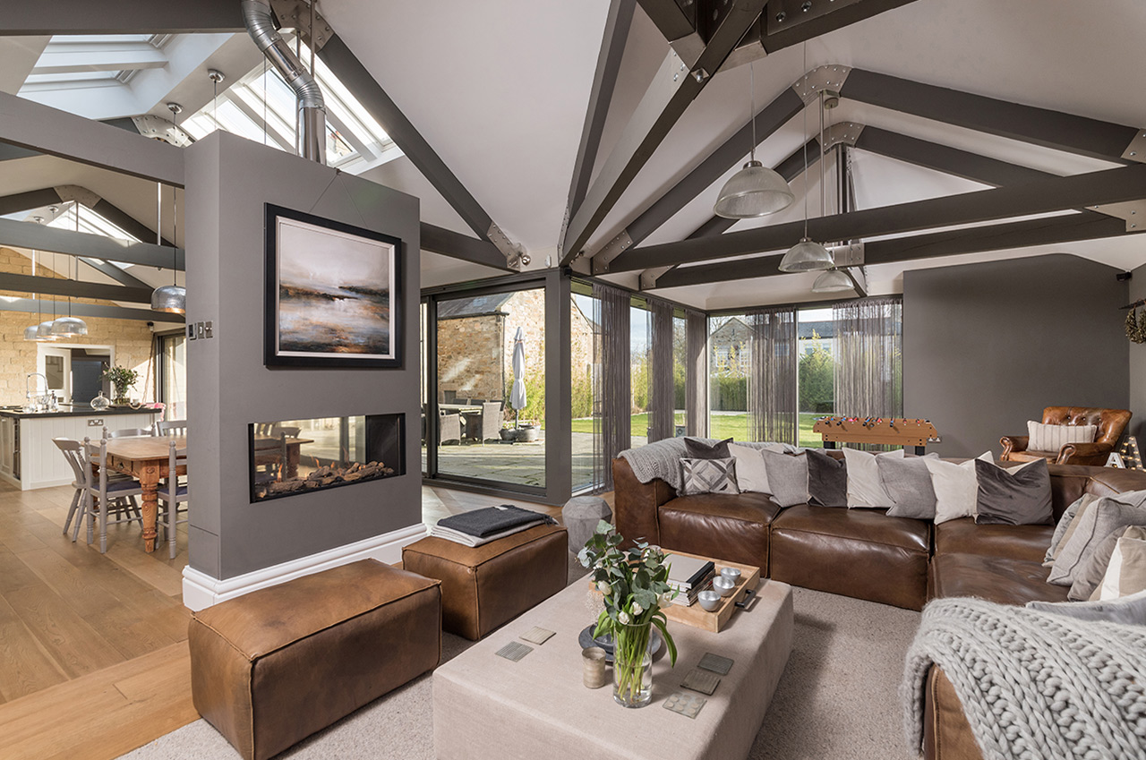 Interior of an open plan kitchen living space with fireplace and exposed modern beams