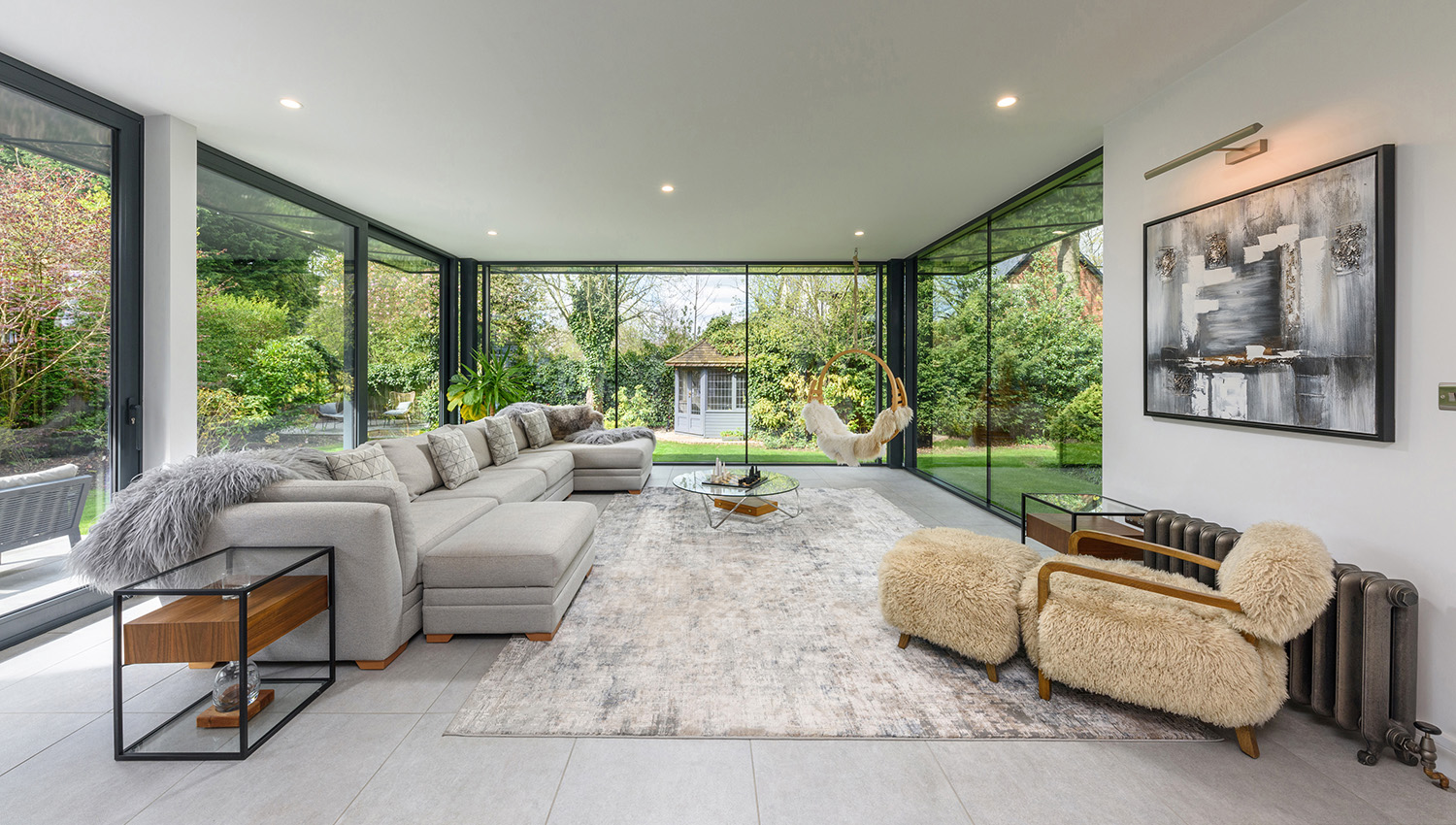 Interior of a garden room with glazed walls and modern furniture overlooking gardens